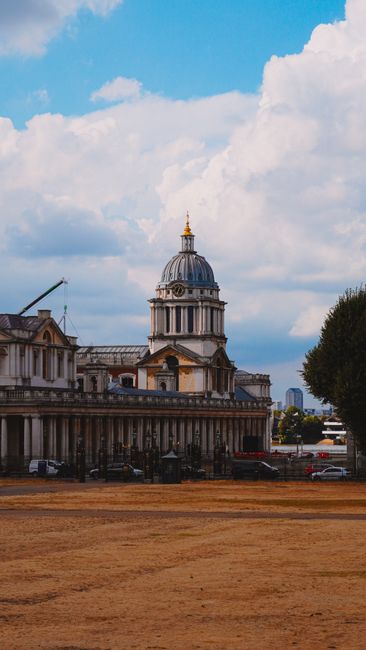 A broad view of a historic building with classical architecture, featuring a prominent dome topped with a gold ornament, situated under a partly cloudy sky. The building's facade shows detailed stonew