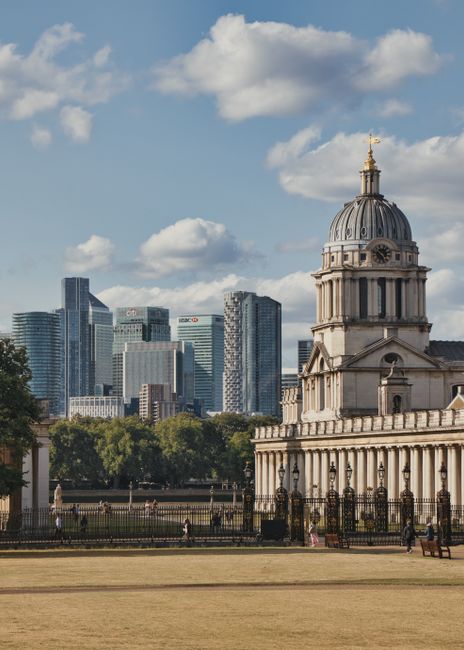 A broad view of a historic building with classical architecture, featuring a prominent dome topped with a gold ornament, situated under a partly cloudy sky. The building's facade shows detailed stonew
